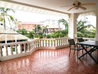 Spacious covered balcony with outdoor furniture and ceiling fan, overlooking a view with palm trees.