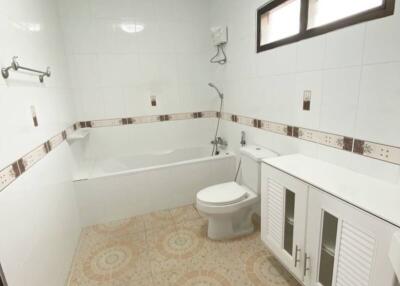 Modern bathroom with tiled walls and floor, storage cabinets, toilet, bathtub with showerhead, and small windows