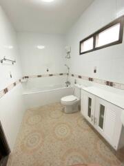 Modern bathroom with tiled walls and floor, storage cabinets, toilet, bathtub with showerhead, and small windows
