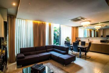 Modern living room with large sectional sofa, dining area, and floor-to-ceiling windows