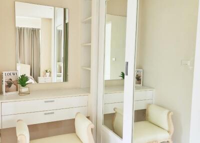 A cozy and elegant vanity area in the bedroom with a mirror, beige upholstered chair, and built-in wardrobe with sliding mirrors.