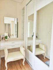 A cozy and elegant vanity area in the bedroom with a mirror, beige upholstered chair, and built-in wardrobe with sliding mirrors.