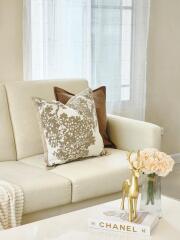 Cozy living room with decorative pillows, white sofa, golden deer statue, Chanel book, and flowers