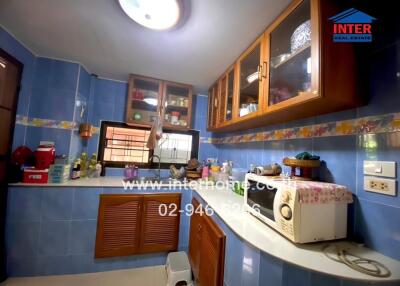 Small kitchen with blue tiles, wooden cabinets and various appliances