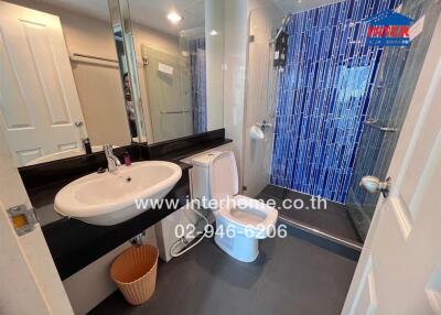 Modern bathroom with white sink and toilet, blue tile accent wall, and glass shower enclosure