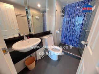 Modern bathroom with white sink and toilet, blue tile accent wall, and glass shower enclosure