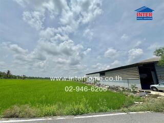 View of an open field with a warehouse and a road, under a cloudy sky