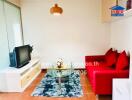 Bright and cozy living room with a red sofa, TV, glass coffee table, and a modern pendant light.