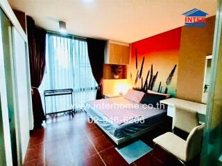 Well-lit bedroom with bed, wardrobes, desk, chair, and large window with sheer curtains.