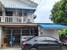 Two-story house with a striped blue and white awning and a parked car.