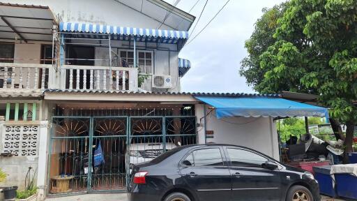 Two-story house with a striped blue and white awning and a parked car.