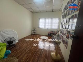 Bedroom with wooden floor, fan, photos on the wall, and a website watermark