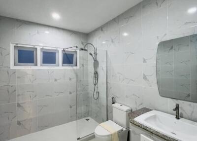 Modern bathroom with marble tiles, glass-enclosed shower, toilet, and vanity