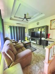 Living room with beige recliner chairs, large TV, ceiling fan, and natural light