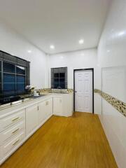 Modern kitchen with wooden flooring, white cabinets, and two windows