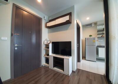 Modern living area with wall-mounted shelves, TV, and visible kitchenette