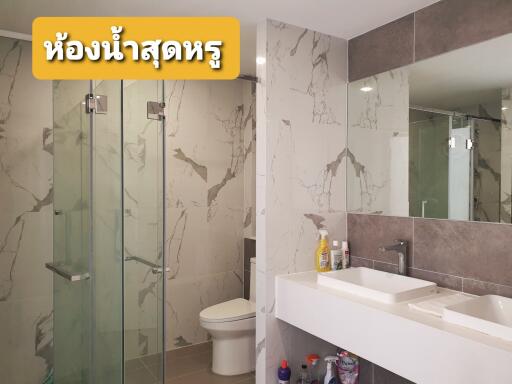 A modern bathroom with a large mirror, double sinks, and a glass shower