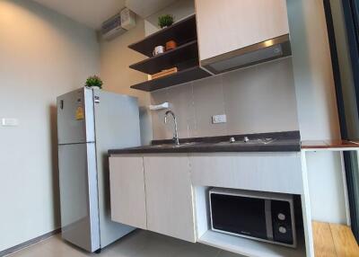 Modern compact kitchen with wooden cabinets, a stainless steel refrigerator, microwave, and a built-in stovetop