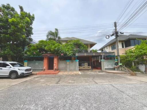 Front view of a multi-story residential house with driveway, carport, and garden.