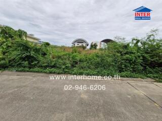 Vacant plot of land with surrounding greenery and nearby structures