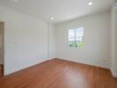 Bright and spacious empty bedroom with wooden floors and a window.