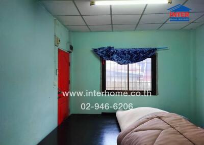 Simple bedroom with a one-bed setup, green walls, and a barred window with a blue curtain