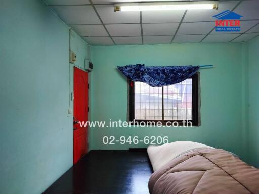 Simple bedroom with a one-bed setup, green walls, and a barred window with a blue curtain