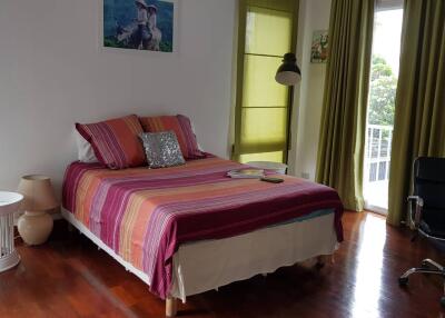Bedroom with colorful bed, green curtains, and wooden floor