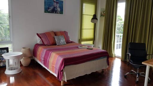 Bedroom with colorful bed, green curtains, and wooden floor