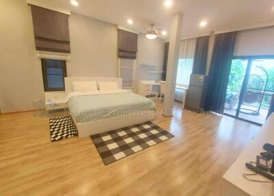 Spacious bedroom with a bed, wooden flooring, and a sliding glass door to the balcony