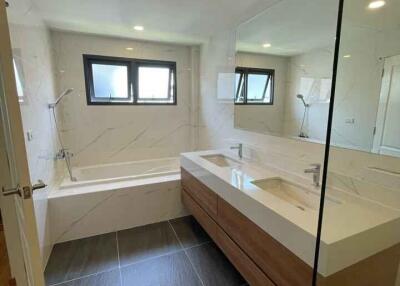 Modern bathroom with large mirror, double sink, bathtub, and windows