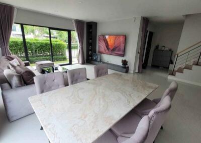 Spacious living room with large marble dining table, cozy sofa set, flat screen TV, and large windows with garden view.