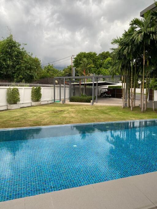 Outdoor pool with a lush garden and a covered parking area