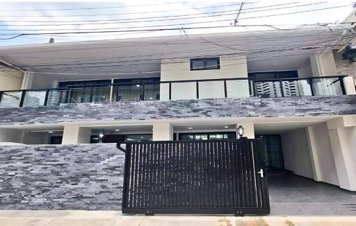 Front exterior view of a modern building with a black gate and stone facade