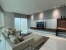 Modern living room with large windows, light grey sofa, TV, and stylish decor