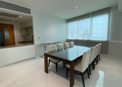Modern dining room with a glass-top table and eight white upholstered chairs, adjacent to an open kitchen