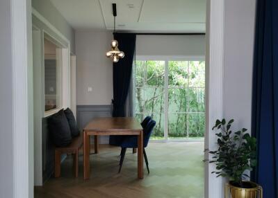 Dining area with a wooden table and chairs, view of greenery through large windows.