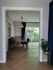 Dining area with a wooden table and chairs, view of greenery through large windows.