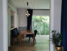 Dining area with a wooden table and chairs, view of greenery through large windows.