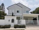 Front view of a modern two-story house with a gated entrance and carport