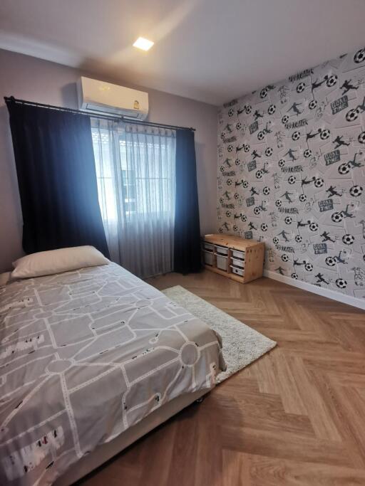 Bedroom with a single bed, patterned wall, wooden floor, and large window with curtains