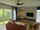 Modern living room with large windows, wall-mounted TV, air conditioner, ceiling fan, and comfortable seating