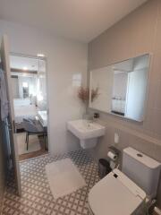 Modern bathroom with sink, mirror, toilet, and view into bedroom