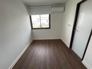 Small, minimalistic bedroom with a wooden floor, window, and white walls