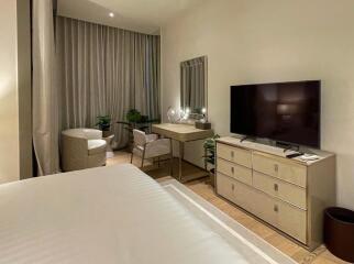 Well-lit bedroom with a bed, TV, dresser, and vanity desk with chair