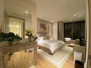 Modern bedroom with a large bed, nightstands, plants, and a seating area