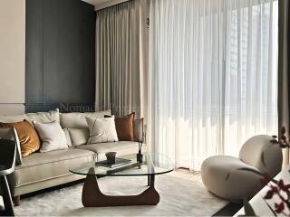 Modern living room with gray sofa, glass coffee table, and large windows with sheer curtains