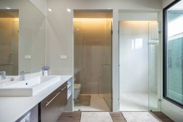 Modern bathroom with double sink vanity, glass-enclosed shower, and large window