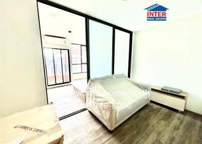 A modern bedroom with large sliding glass doors, an air conditioning unit, and wooden flooring