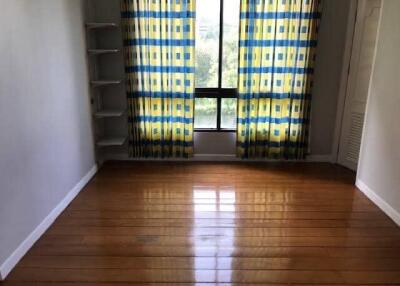Empty room with hardwood flooring, window with patterned curtains, and built-in shelving